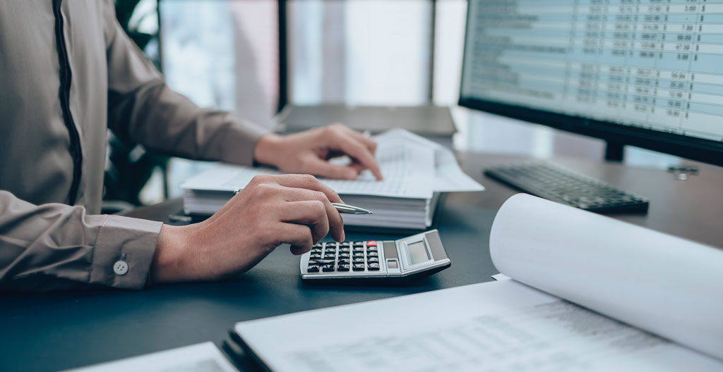 Gros plan sur des mains en train de taper sur un clavier d'ordinateur portable moderne avec un graphique financier flouté visible en arrière-plan sur l'écran