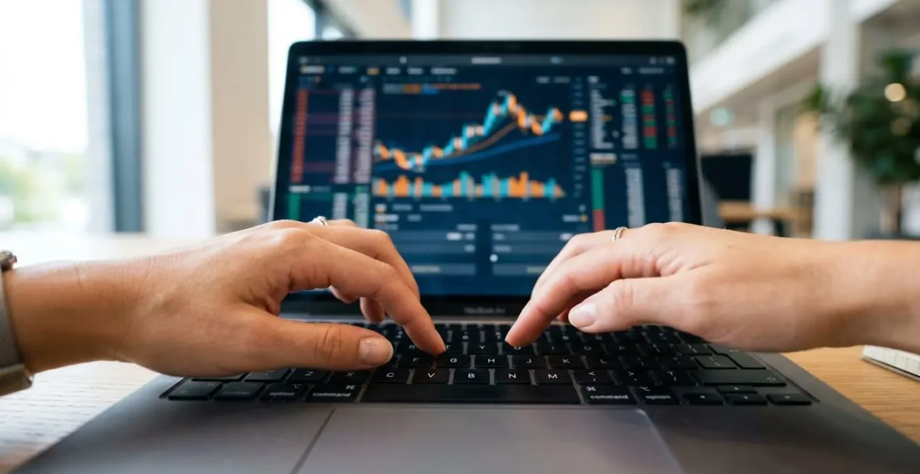 Gros plan sur des mains en train de taper sur un clavier d'ordinateur portable moderne avec un graphique financier flouté visible en arrière-plan sur l'écran